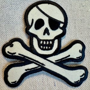 May include: White embroidered skull and crossbones patch with black outlines. The skull has a black eye patch and a white bandana.