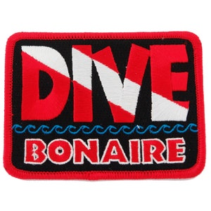 May include: Red and white embroidered patch with the word "DIVE" in a scuba diving flag design. Below the word "DIVE" is a row of blue waves and the word "BONAIRE" in red.
