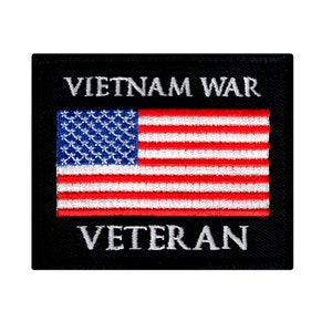 Może przedstawiać: Prostokątna czarna naszywka z haftowaną flagą amerykańską. Flaga ma czerwono-białe paski i niebieskie pole z gwiazdami. Napisy "VIETNAM WAR" i "VETERAN" są wyhaftowane na biało.