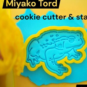 May include: A blue and yellow frog cookie cutter and stamp set on a blue surface. The text "Miyako Tord" and "cookie cutter & stamp" are at the top. The text "STL DOWNLOAD" is at the bottom.
