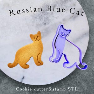 May include: A baked cookie and a purple cookie cutter in the shape of a cat, labeled "Russian Blue Cat." The cookie is golden brown with a smiling face. The cutter is a light purple color. The text "Cookie cutter&stamp STL" is also present.