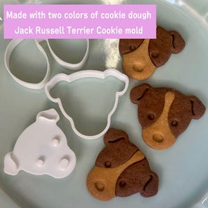 May include: A Jack Russell Terrier cookie mould and cookies made with two colours of cookie dough. The cookies are brown and tan, shaped like a dog's head. The white plastic mould is in the shape of a dog's head and two other shapes. Text on the image reads: Made with two colours of cookie dough Jack Russell Terrier Cookie mould.