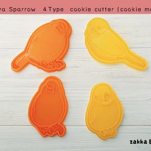 May include: Four cookie cutters shaped like sparrows. Two are orange and two are yellow. The cutters are on a white wooden surface. The text "Java Sparrow 4 Type cookie cutter (cookie mold)" is at the top of the image. The text "zakka Bianca" is at the bottom of the image.