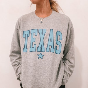 May include: Gray sweatshirt with a blue and white "TEXAS" graphic on the front. The sweatshirt has a crew neck and long sleeves.