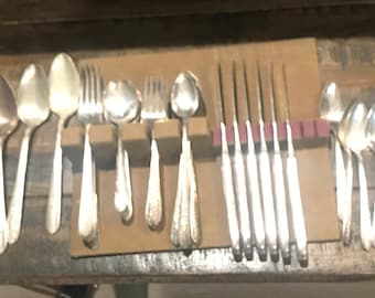 May include: A collection of silver-colored flatware, including spoons, forks, and knives, arranged in a wooden drawer. The utensils are neatly organized, with the knives placed in a separate holder. The silverware has a shiny, reflective surface.