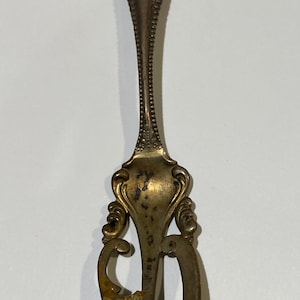 Pode incluir: Um garfo vintage prateado com um design ornamentado e três dentes. O garfo tem um cabo decorativo com um padrão floral e um monograma.