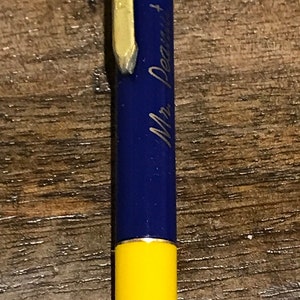 以下が含まれることがあります： 青いシルクハットをかぶったピーナッツのキャラクターが付いた黄色と青のペン。ペンには「Mr. Peanut」の文字が書かれています。