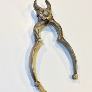 Könnte beinhalten: Silberfarbener Nussknacker mit dekorativem Design. Der Nussknacker hat einen Klappkiefer und einen dekorativen Griff.