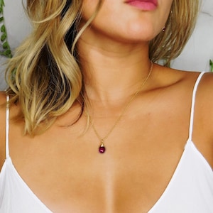 May include: A gold chain necklace with a small, round, dark red gemstone pendant.