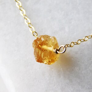 May include: A gold chain necklace with a raw, faceted, yellow citrine gemstone pendant.