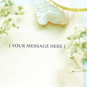 Puede incluir: Una tarjeta color crema con el texto "[ YOUR MESSAGE HERE ]" est&aacute; rodeada de flores blancas y una concha sobre un fondo azul claro. Una cinta dorada es visible cerca de la concha. La imagen tiene una est&eacute;tica suave y aireada.