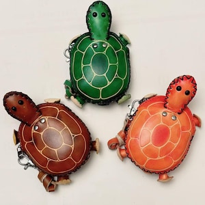 May include: Three leather turtle coin purses in green, brown, and orange. Each purse has a small key chain attached.