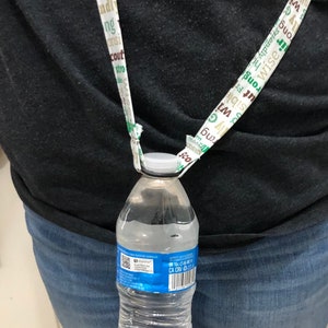 May include: A clear plastic water bottle with a blue label that says "ONTOS CH-ME 50 CA CRV 10" is attached to a white lanyard with green and brown text. The lanyard is worn around a person's neck.