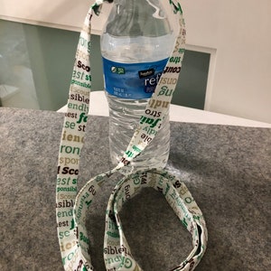 May include: A white fabric lanyard with green and brown text that says "Scout", "est", "sible", "friendly", "strong", "responsible", "best", "iron", "and"  wrapped around a clear plastic water bottle.