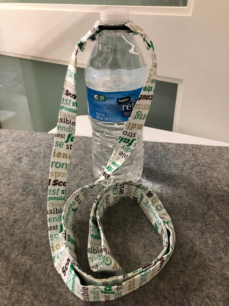 May include: A white fabric lanyard with green and brown text that says "Scout", "est", "sible", "friendly", "strong", "responsible", "best", "iron", "and"  wrapped around a clear plastic water bottle.