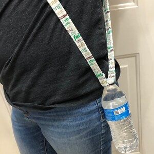 May include: A white lanyard with green and brown text that says "scout", "strong", "wise", "fair", "kindly", "honorable", "brave", "trustworthy", "loyal", "helpful", "friendly", "courteous", "responsible", and "obedient". The lanyard is holding a clear plastic water bottle.
