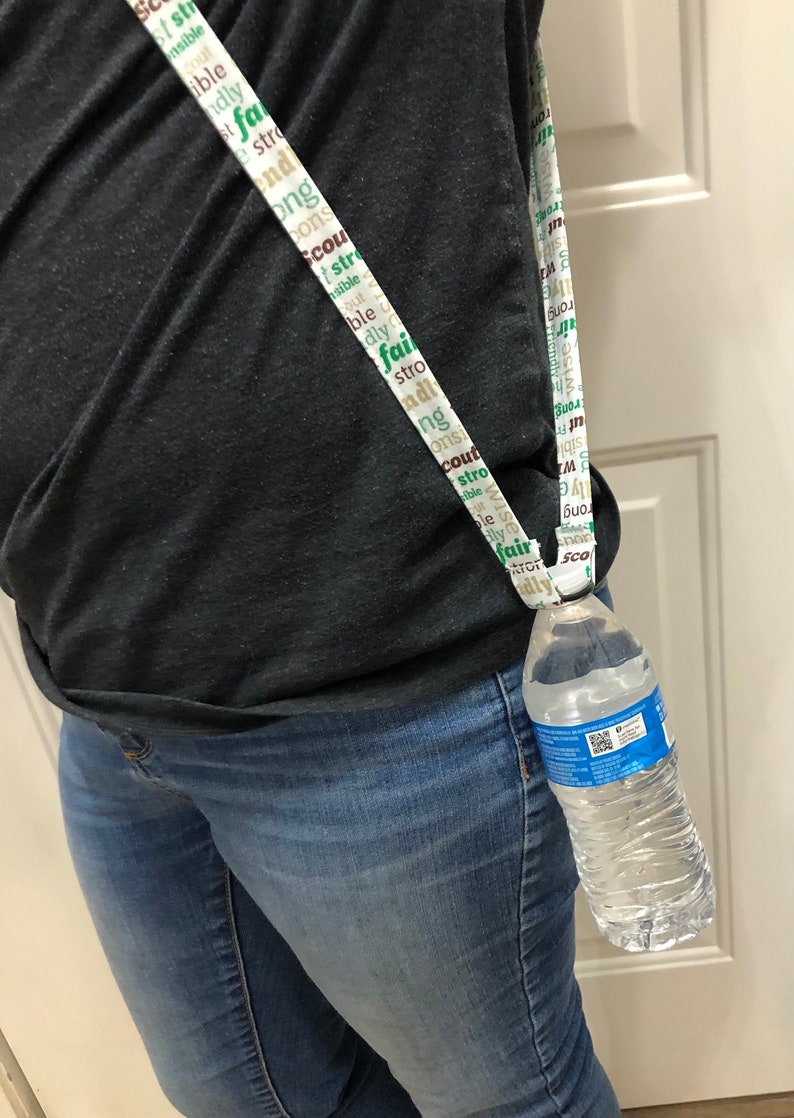 May include: A white lanyard with green and brown text that says "scout", "strong", "wise", "fair", "kindly", "honorable", "brave", "trustworthy", "loyal", "helpful", "friendly", "courteous", "responsible", and "obedient". The lanyard is holding a clear plastic water bottle.