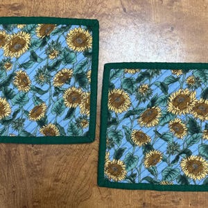 May include: Two square blue and green quilted pot holders with a sunflower pattern.