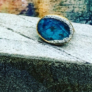 Puede incluir: Un anillo ovalado de color azul turquesa con un engaste de oro y un borde de peque&ntilde;as piedras blancas.