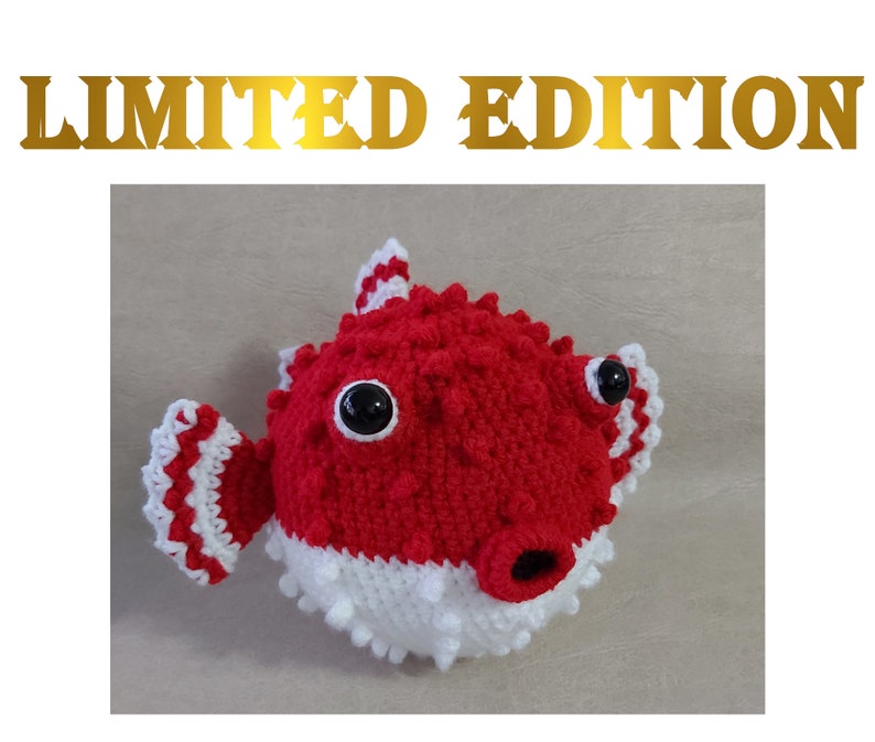 Puede incluir: Un juguete de peluche de pez globo rojo y blanco tejido a crochet con ojos negros. El juguete es una edici&oacute;n limitada.
