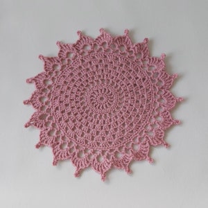 May include: A pink crocheted doily with a circular design and a scalloped edge.