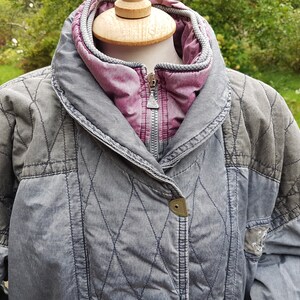 May include: A grey quilted jacket with a pink lining and a zip closure. The jacket has a diamond-shaped quilted pattern and a button on the front.