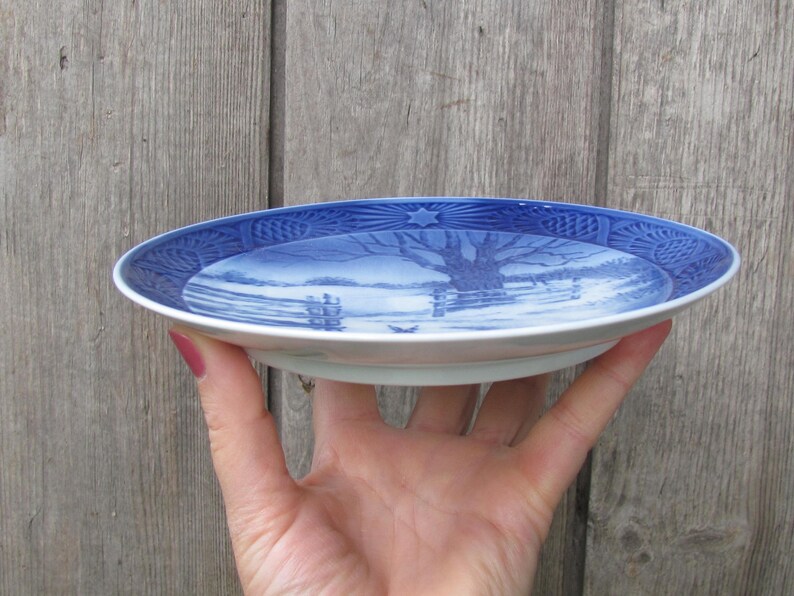 May include: A blue and white ceramic plate with a winter scene design. The plate features a tree, a river, and a snowy landscape.