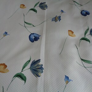 May include: White fabric with a repeating pattern of blue and yellow flowers. The flowers are stylized and have a watercolor look.