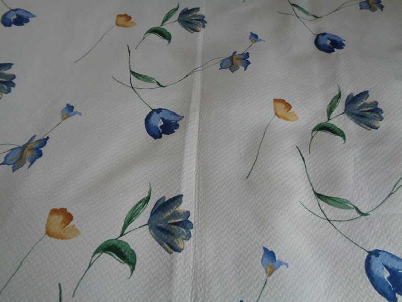 May include: White fabric with a repeating pattern of blue and yellow flowers. The flowers are stylized and have a watercolor look.