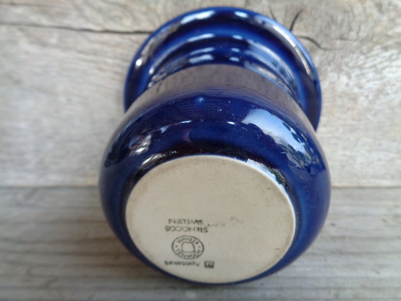 May include: A blue ceramic mug with a white bottom. The bottom of the mug has the text "STINCOOS SWEDEN" and a logo.