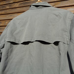 Puede incluir: Una camisa gris de manga larga con cuello abotonado y una solapa en la espalda.