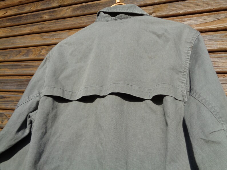 Puede incluir: Una camisa gris de manga larga con cuello abotonado y una solapa en la espalda.