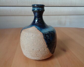 Könnte beinhalten: Eine kleine, runde Keramikvase mit blauer und brauner Glasur. Die Vase hat einen schmalen Hals und einen breiten Boden.