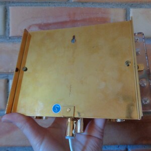 K&ouml;nnte beinhalten: R&uuml;ckansicht einer goldfarbenen Wandleuchte mit einem klaren Glasschirm. Die Leuchte hat einen kleinen blauen Aufkleber auf der R&uuml;ckseite mit dem Buchstaben "S" darauf.
