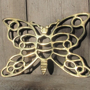 May include: A gold-colored metal butterfly-shaped trivet with a decorative, intricate design. The trivet is made of a thin, openwork metal and has a delicate, airy appearance.