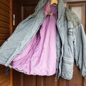 May include: A blue denim jacket with a purple quilted lining. The jacket has a zip closure and a patch on the left sleeve.