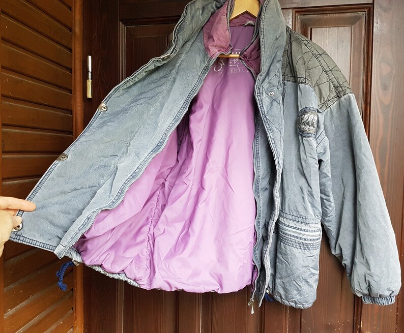 May include: A blue denim jacket with a purple quilted lining. The jacket has a zip closure and a patch on the left sleeve.