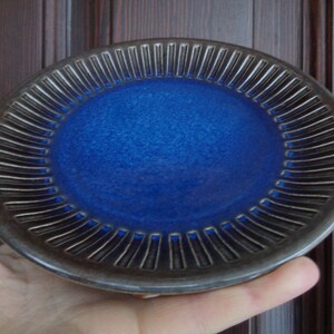 May include: A small, blue ceramic plate with a dark gray rim and a decorative, ribbed pattern around the edge.