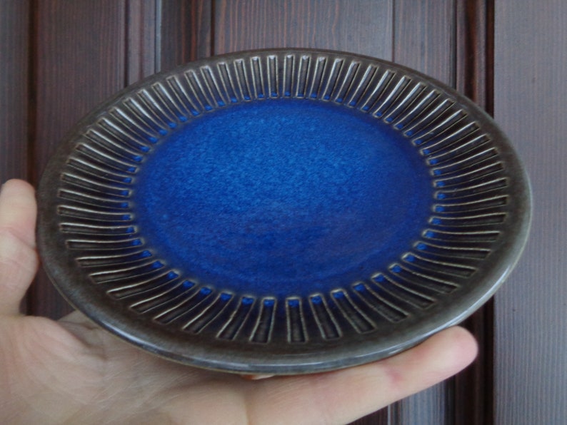 May include: A small, blue ceramic plate with a dark gray rim and a decorative, ribbed pattern around the edge.