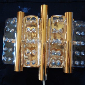 K&ouml;nnte beinhalten: Goldene Wandleuchte mit vier klaren Glasplatten, jede mit einem strukturierten Muster. Die Leuchte hat ein modernes Design und w&auml;re eine gro&szlig;artige Erg&auml;nzung f&uuml;r jedes Zuhause.