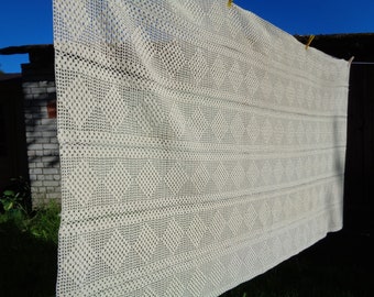 May include: A white crocheted tablecloth with a diamond pattern hangs on a clothesline.