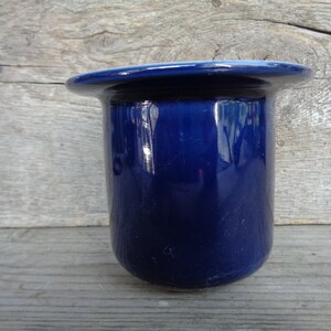 May include: A dark blue ceramic toothbrush holder with a smooth, glossy finish.