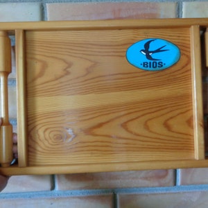 May include: A wooden serving tray with two handles. The tray has a blue oval sticker with a white swallow and the word "BIOS" in white letters.