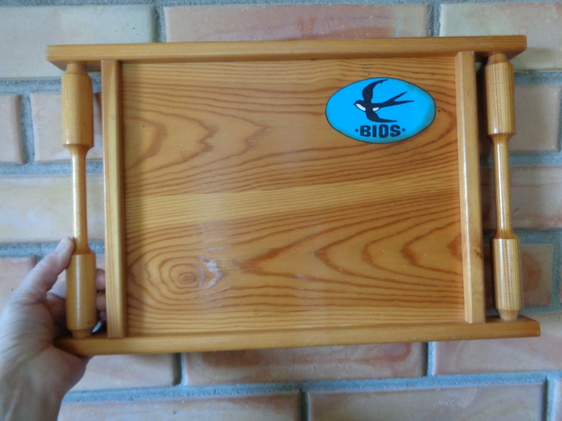 May include: A wooden serving tray with two handles. The tray has a blue oval sticker with a white swallow and the word "BIOS" in white letters.