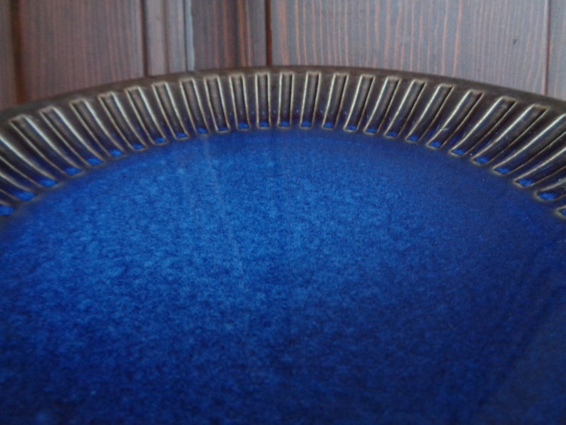 May include: A deep blue ceramic bowl with a textured rim. The bowl has a slightly speckled glaze.