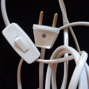 K&ouml;nnte beinhalten: Ein wei&szlig;es Stromkabel mit einem wei&szlig;en Inline-Schalter und einem wei&szlig;en Stecker mit zwei Stiften.