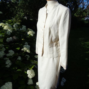 May include: A white linen suit with a mandarin collar and gold trim. The jacket has a button closure and the skirt has a straight silhouette.