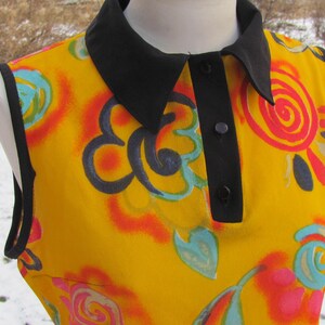 K&ouml;nnte beinhalten: Eine &auml;rmellose gelbe Bluse mit schwarzem Kragen und Kn&ouml;pfen. Die Bluse hat einen bunten abstrakten Druck mit Wirbeln und Blumen.