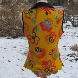 K&ouml;nnte beinhalten: Eine gelbe, &auml;rmellose Weste mit schwarzem Kragen und einem bunten, abstrakten Blumenmuster.