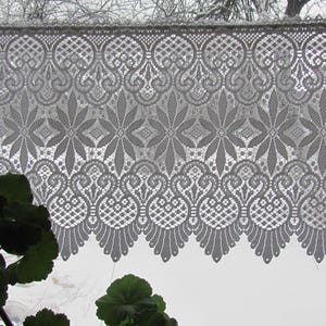 May include: White lace curtain with a delicate floral pattern. The lace is a traditional design with a scalloped edge.